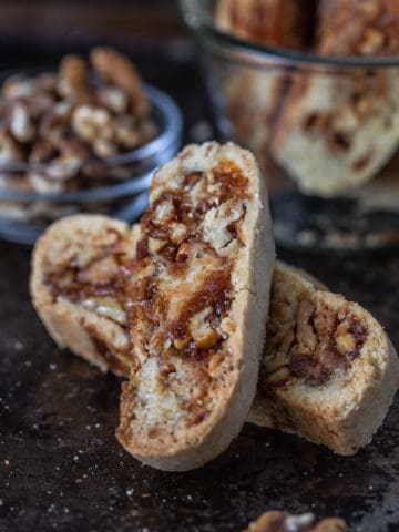 Two walnut praline biscotti on a plate with a bowl of cookies behind.