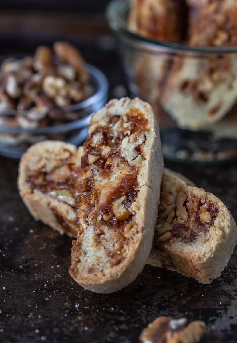 Two walnut praline biscotti on a plate with a bowl of cookies behind.
