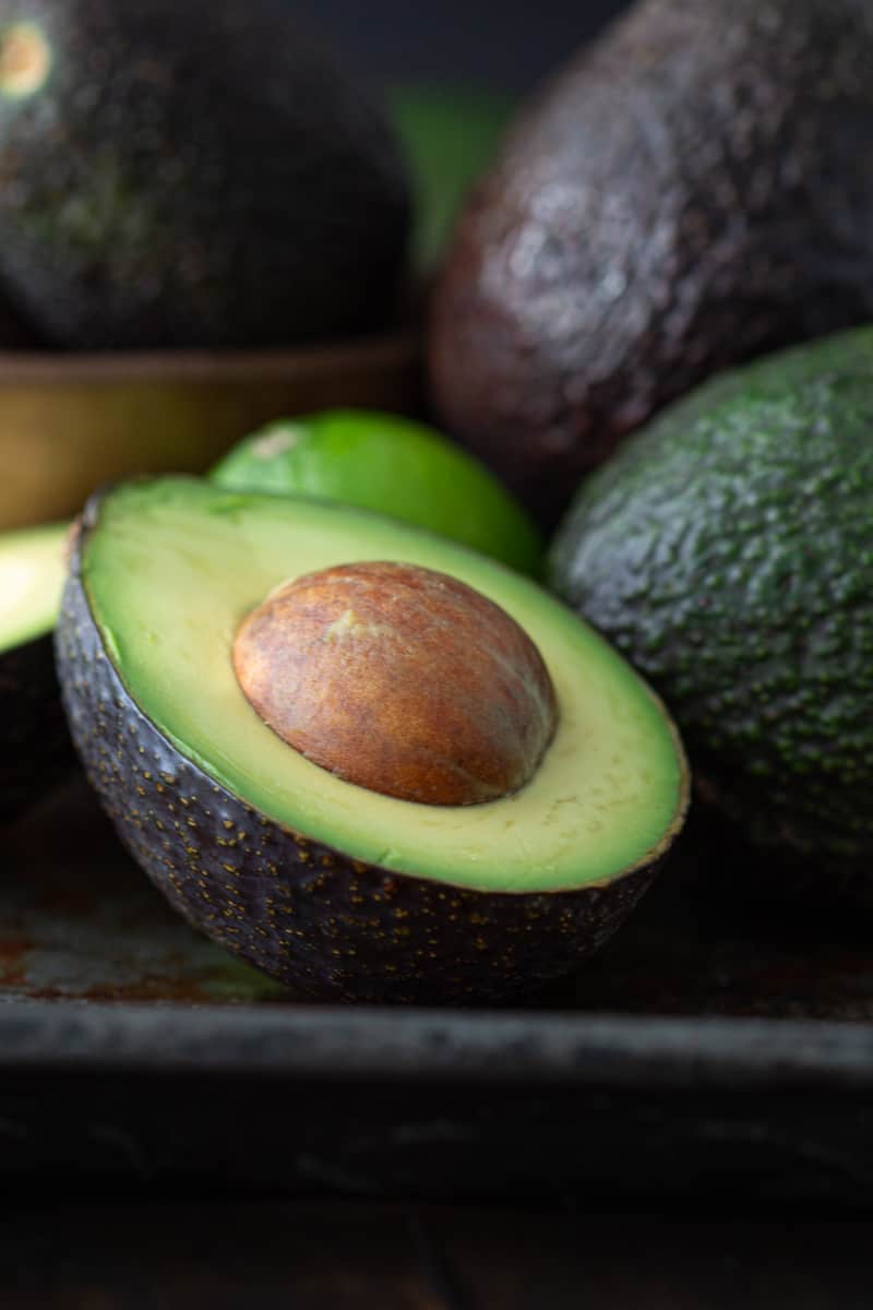 Close up of avocado half with whole avocados on a plate.