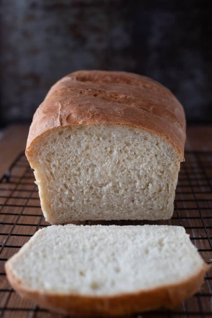 Freshly baked white loaf of white bread with one slice cut off.