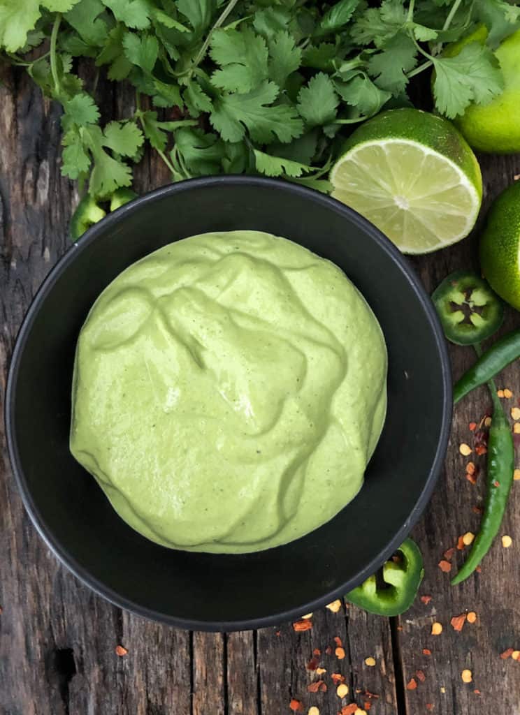 Overhead shot of bright green cashew sauce in a bowl surrounded by limes and green chilies.