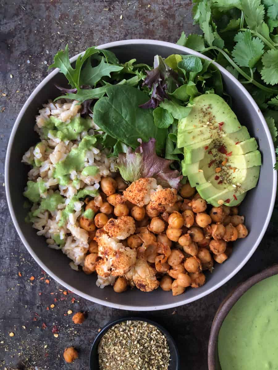 Buddha bowl with cauliflower, chickpeas, avocado and green tahini sauce drizzle.