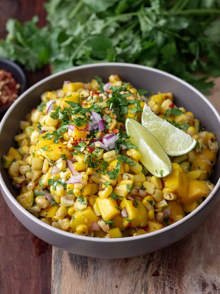 Big bowl of mango corn salsa topped with lime wedges and chopped cilantro.