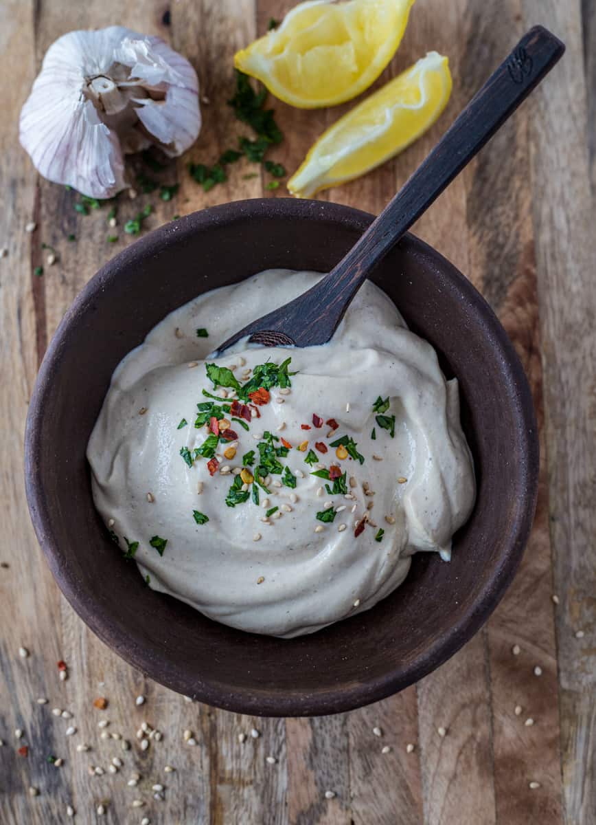 Basic tahini sauce in a bowl with spoon on a board with head of garlic and lemon wedges.