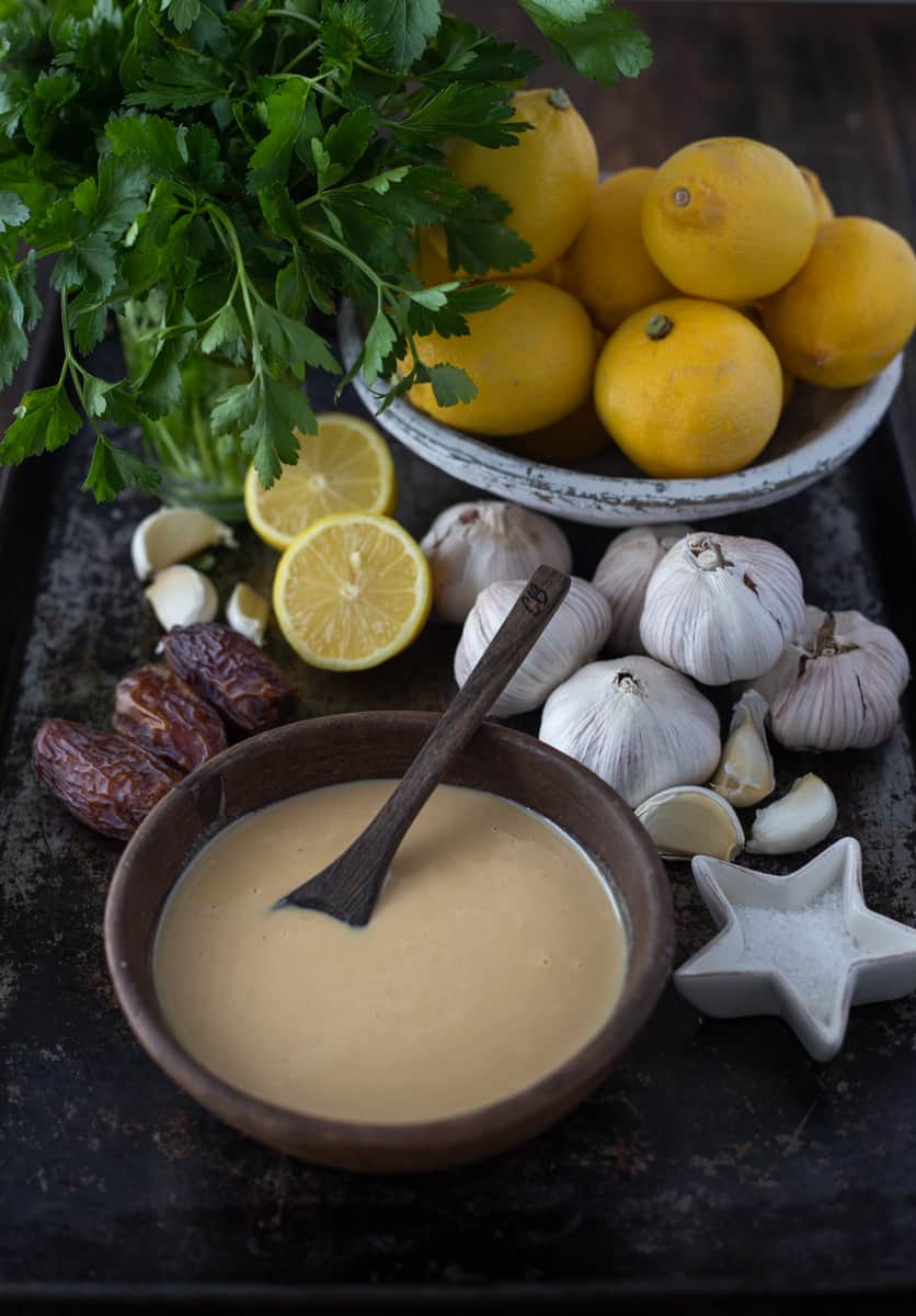 Tray of ingredients for tahini sauce like garlic lemons dates and sauce.