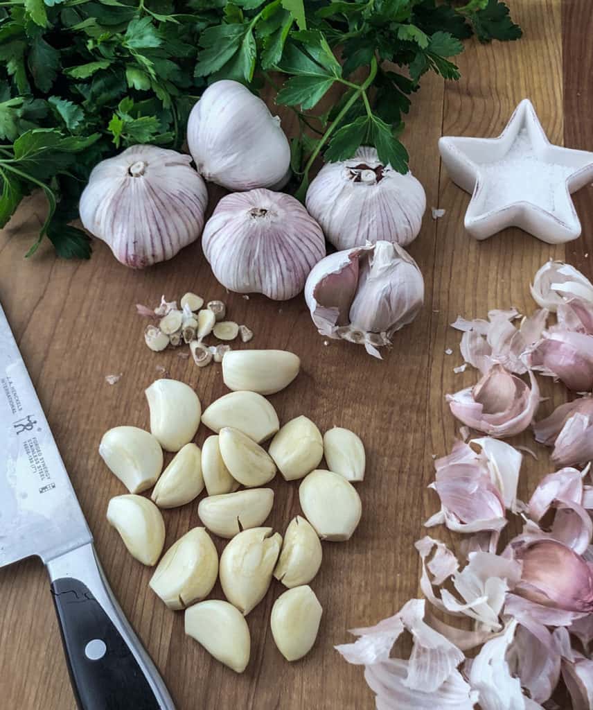 Cutting board with peeled cloves and heads of garlic.