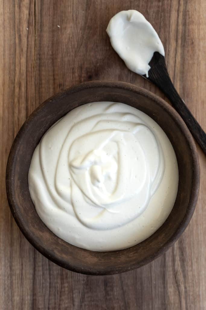 Bowl of cashew cream with spoon on cutting board.