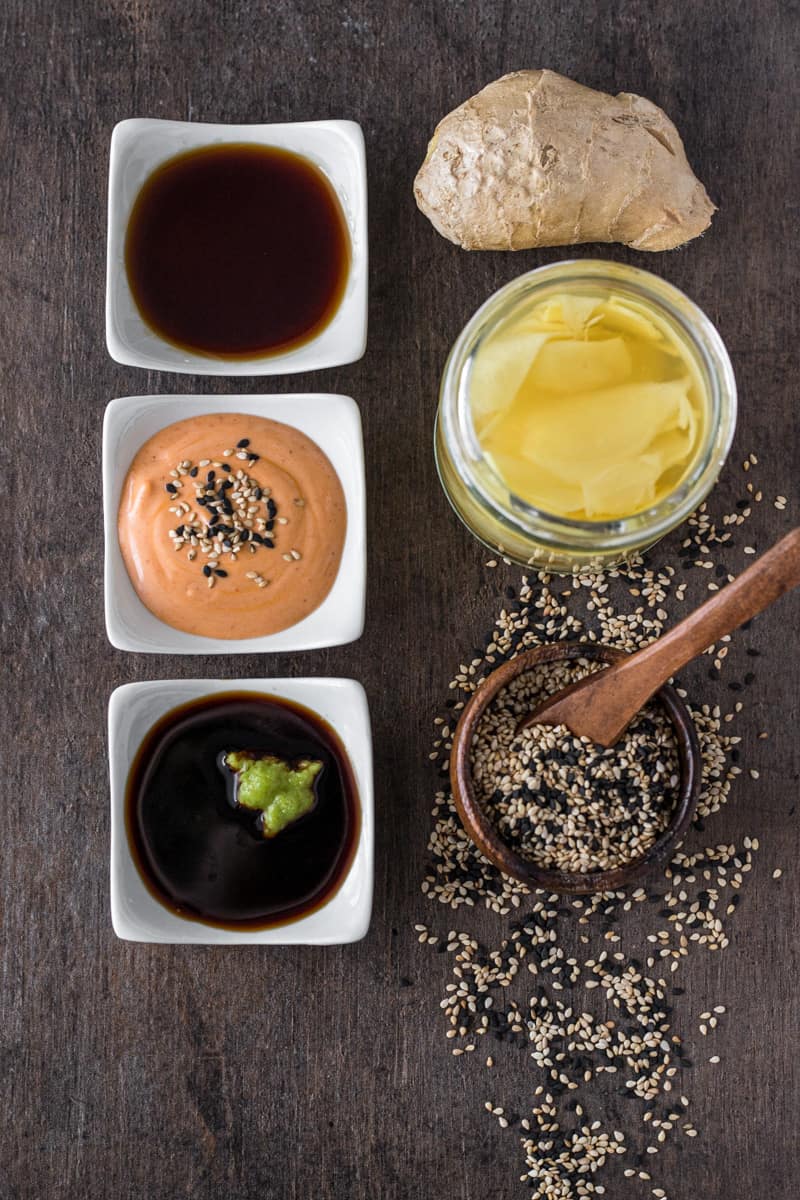 Three bowls of dipping sauce, pickled ginger, and sesame seeds for sushi.