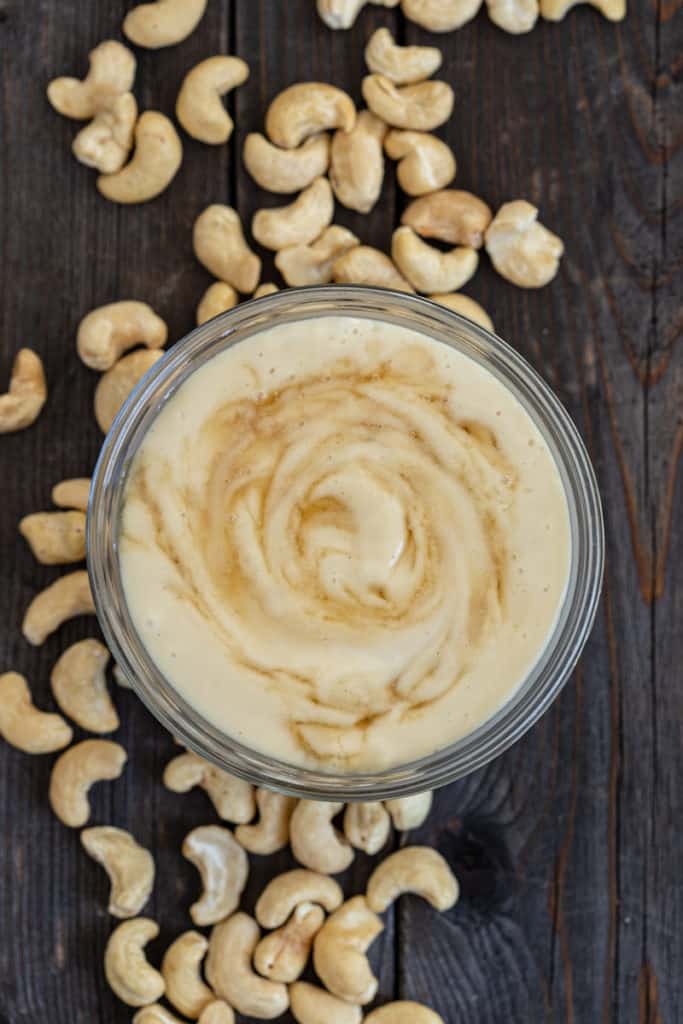 Bowl of maple cashew cream sauce and cashew nuts on a baking tray.