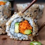 Chopsticks lifting a vegan sushi roll made with carrots and avocado.