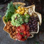 Overhead shot of taco bowl with guacamole, tofu crumble, beans, corn, and tomatoes.