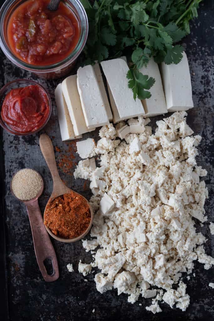 Tofu slices and crumbles on a baking tray with ingredients for vegan tacos.