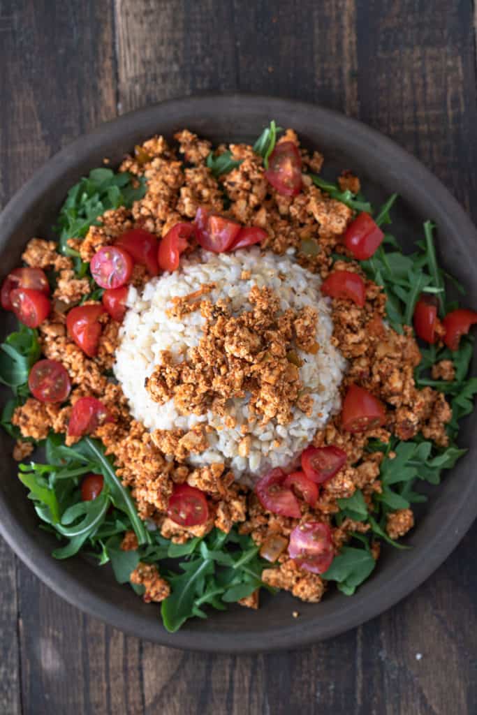 Spicy tofu crumbles on a bed of greens with tomatoes and rice.