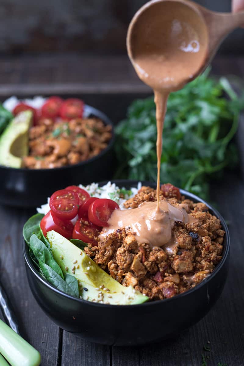 Sweet and spicy tahini sauce being drizzled on vegan taco bowl.