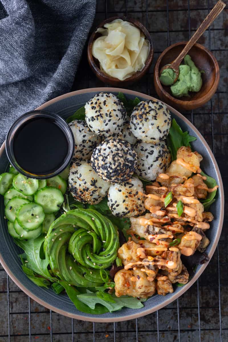 Vegan sushi bowl with tempura mushrooms, rice balls and an avocado rose.