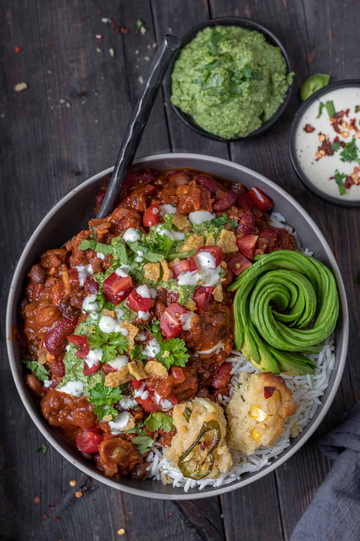 Bowl of best vegan chili served on rice with corn bread and avocado rose.