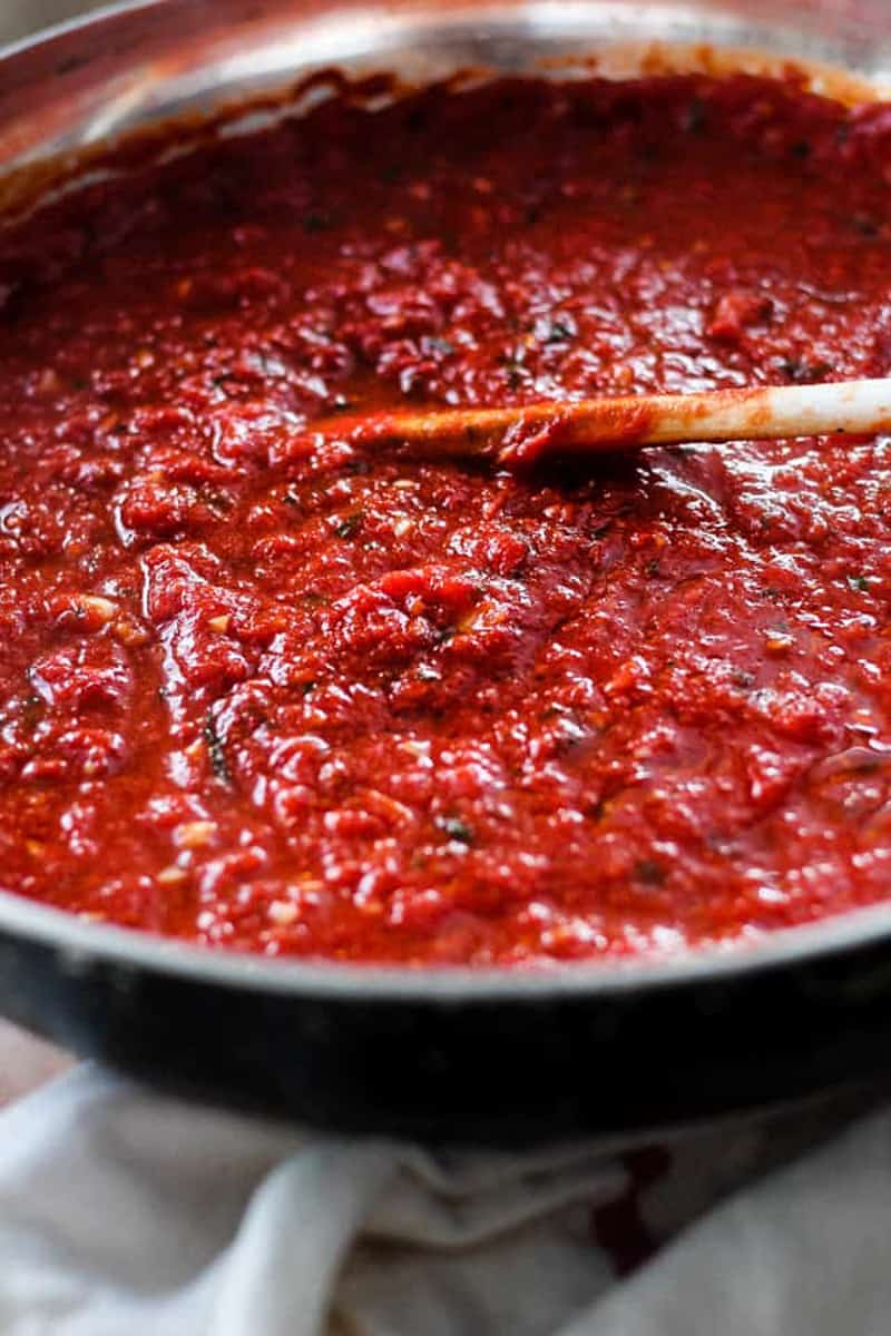 Saucepan of rich red marinara sauce being stirred.