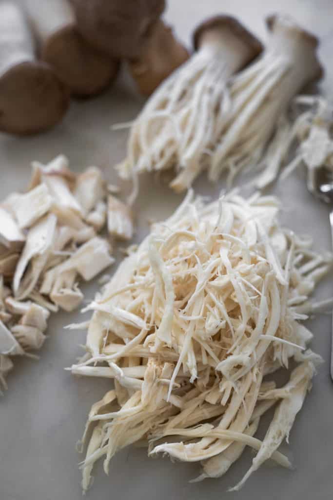 King oyster mushrooms shredded pulled and chunks on cutting board.
