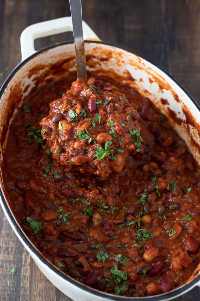 Ladleful of thick chunky vegetarian chili being lifted from Dutch oven.