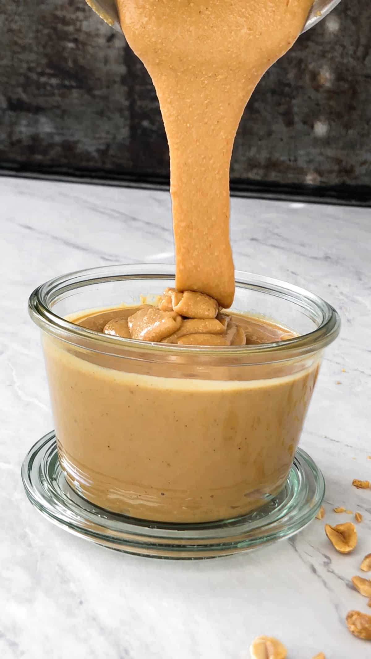 Homemade peanut butter being poured in a jar.