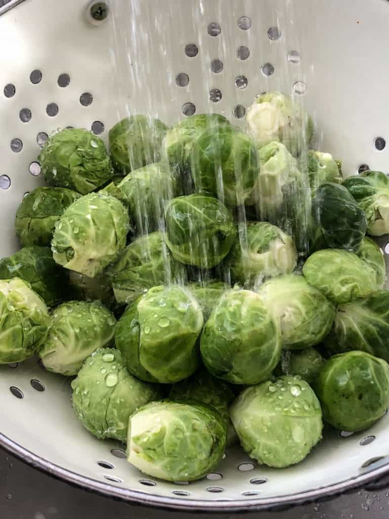 Water showering down on Brussels sprouts in a colander.