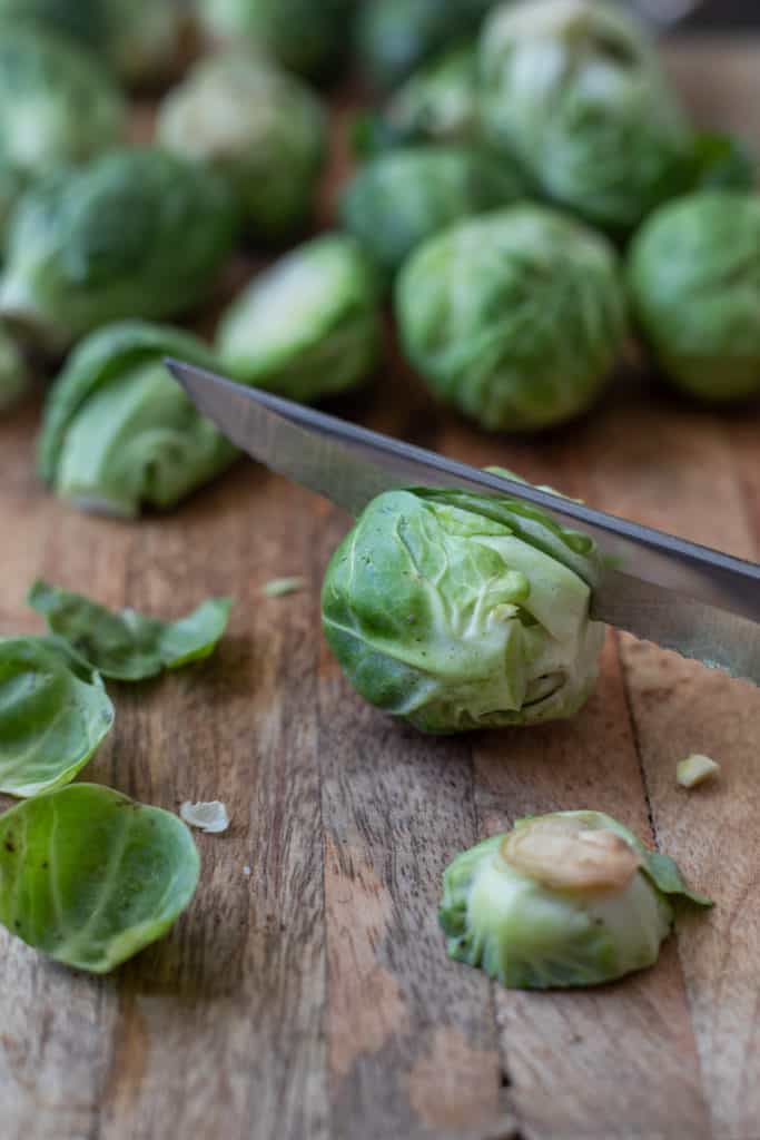 Brussel sprout on cutting board being sliced.