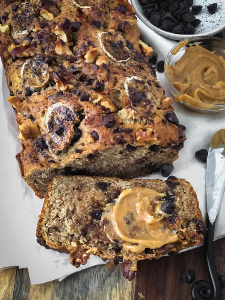 Vegan peanut butter chocolate chip banana loaf with a slice smeared with peanut butter.