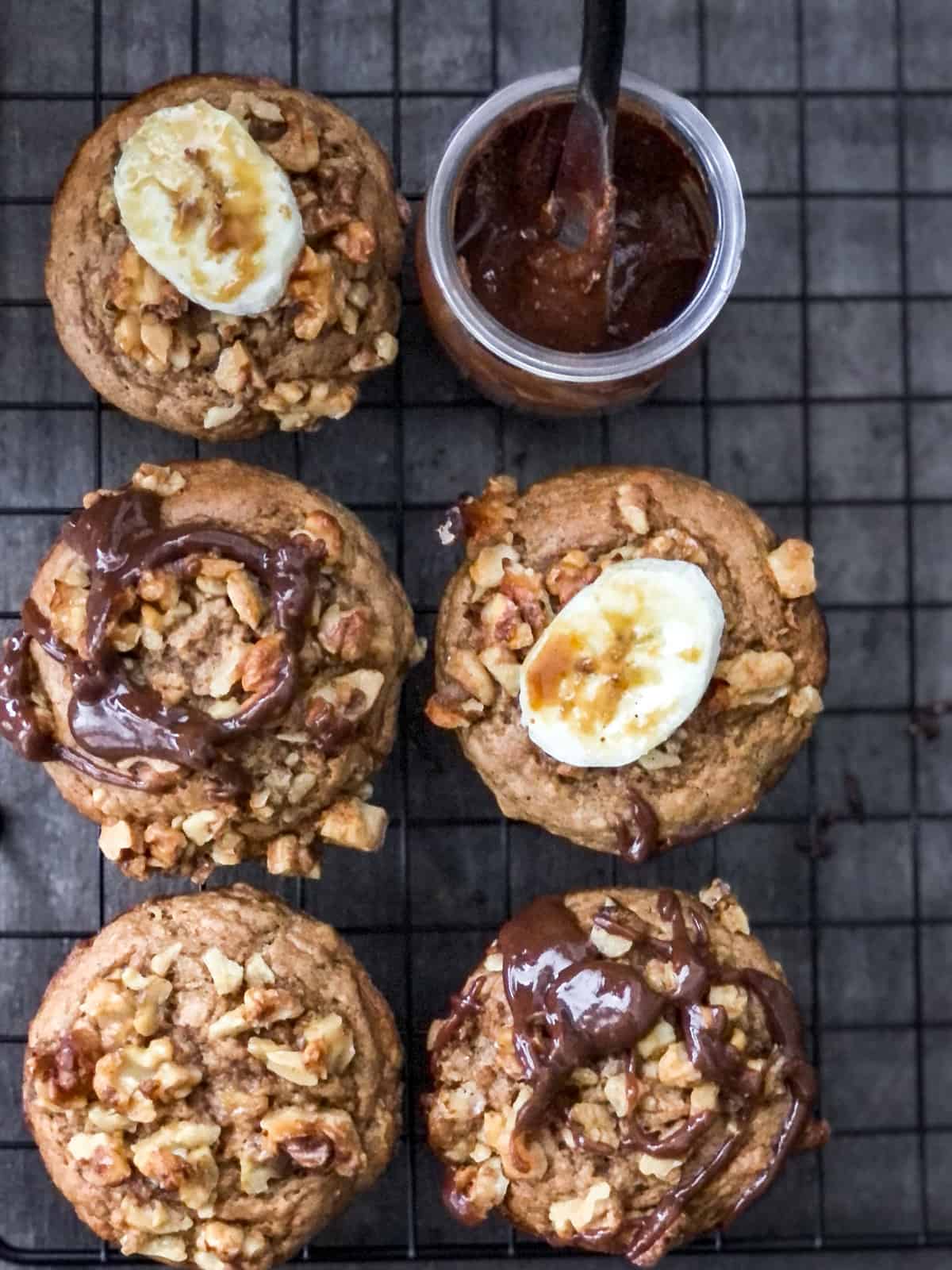 Banana nut muffins topped with banana slice and chocolate drizzled on a cooling rack.