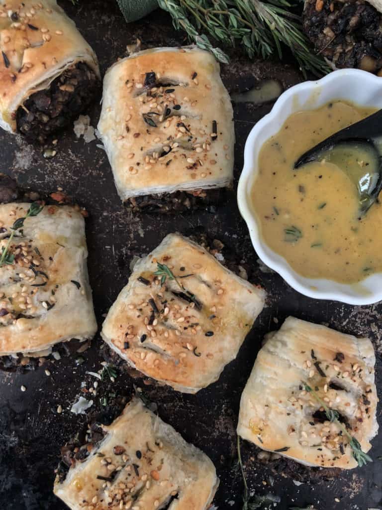 Vegan sausage rolls around a dish of vegan honey mustard sauce.