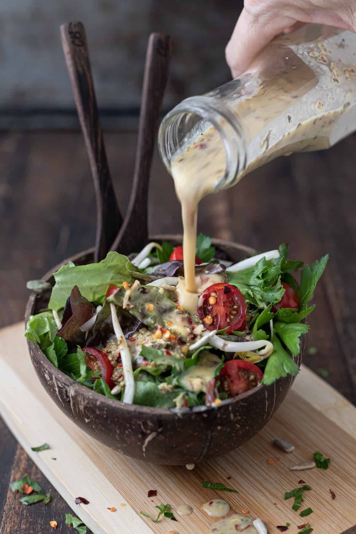 Lemon vinaigrette dressing being poured into a garden salad with tomatoes.