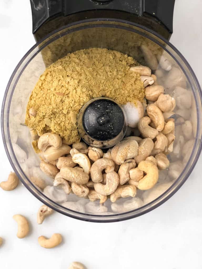 Raw cashews in food processor bowl for vegan parmesan cheese.