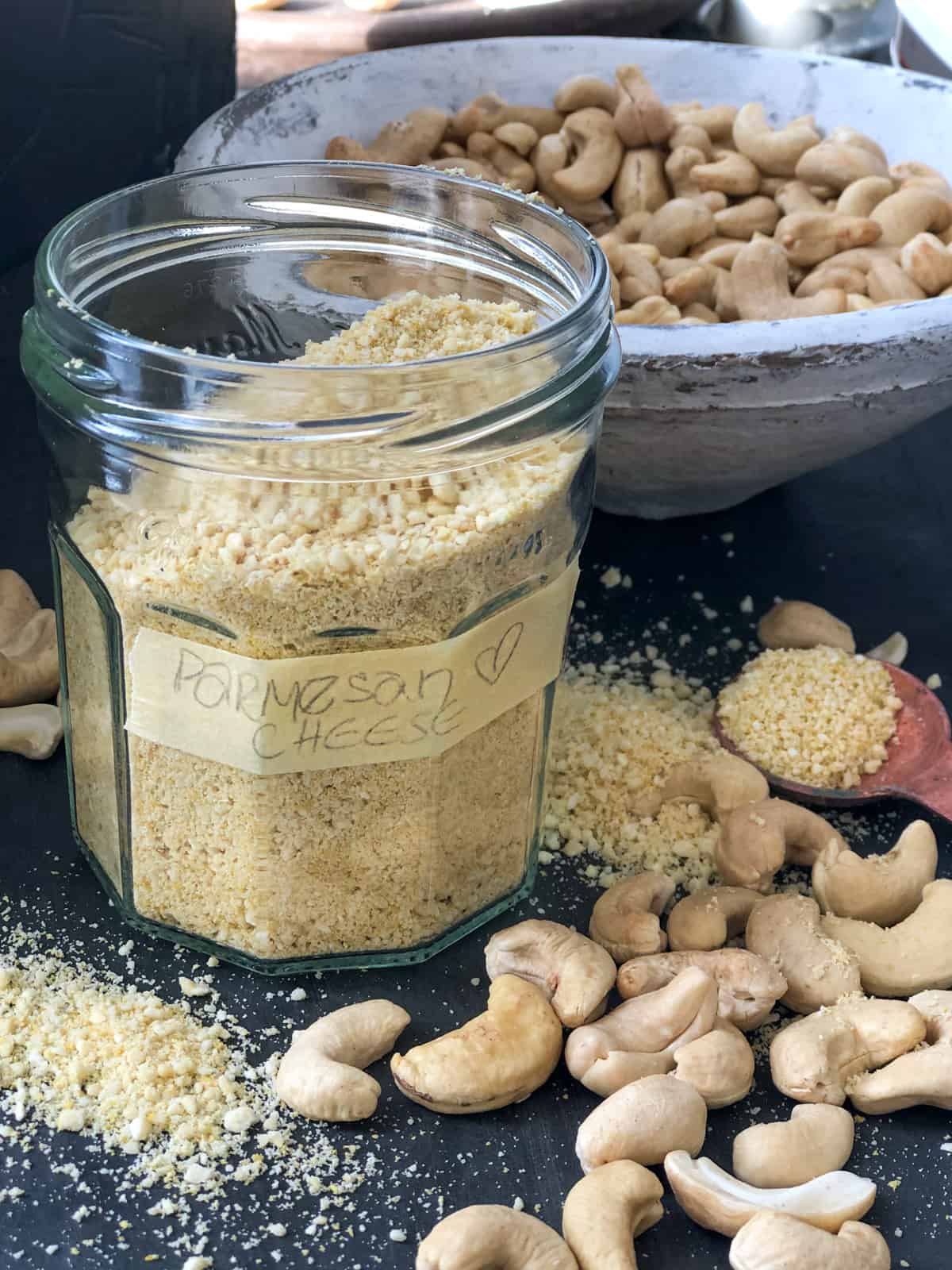 Jar of vegan parmesan cheese and bowlful of cashew nuts on tray.