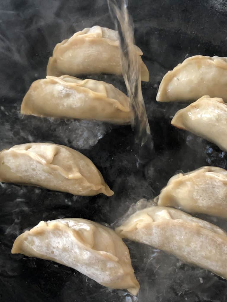 Steaming potstickers in a hot skillet.