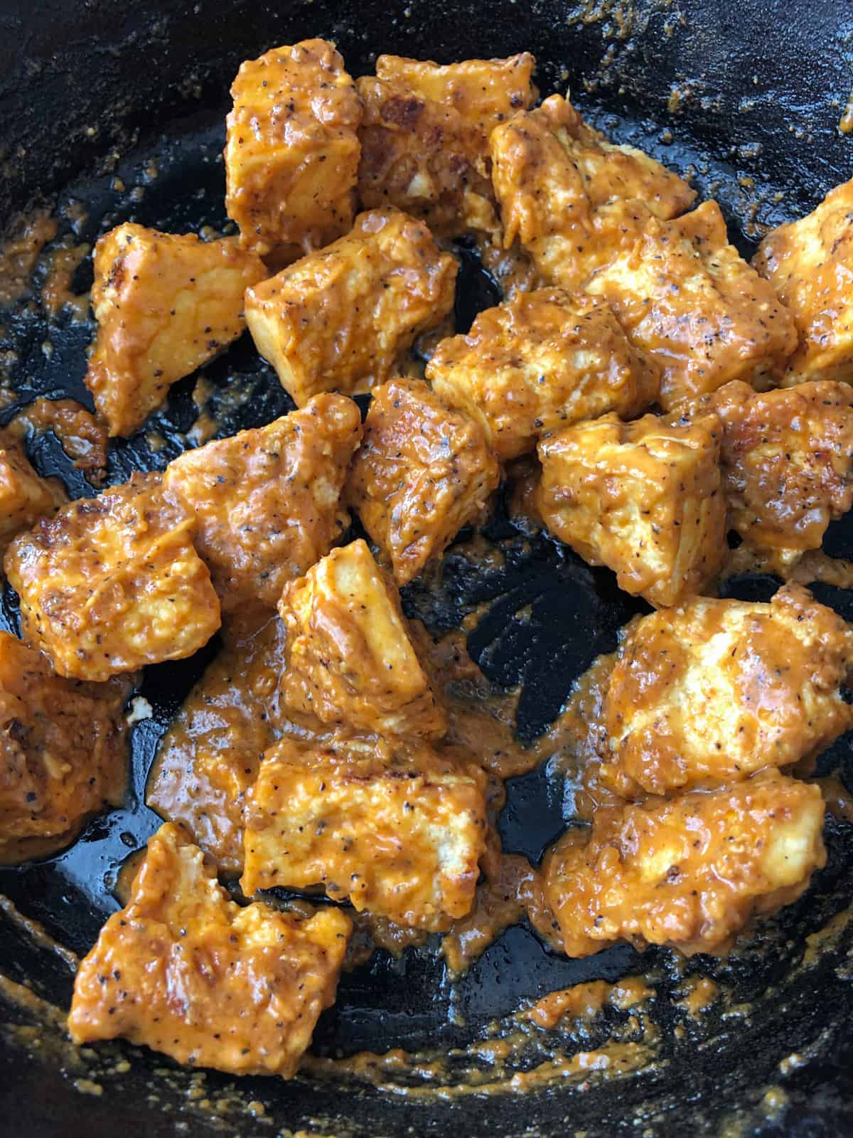 Baked tofu chunks in peanut sauce in a skillet.