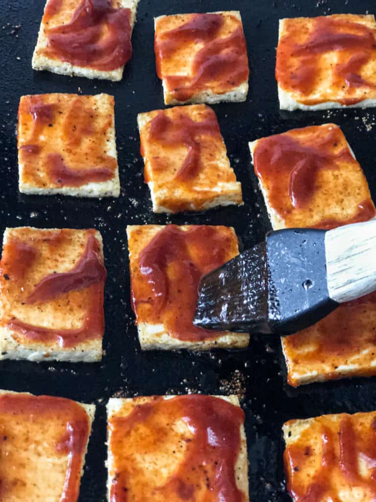 BBQ sauce being brushed on tofu slices.