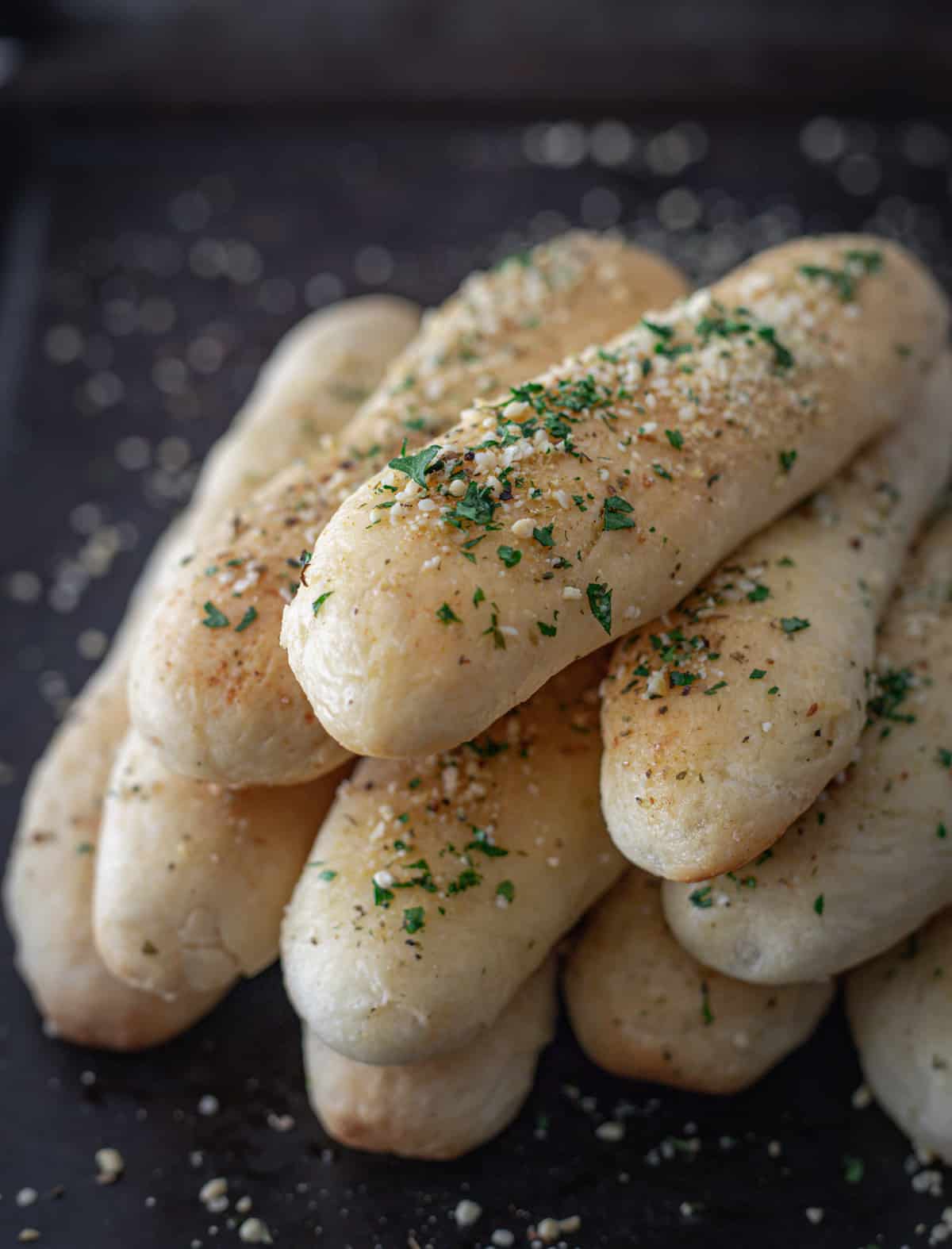 Golden breadsticks piled up on a baking sheet.