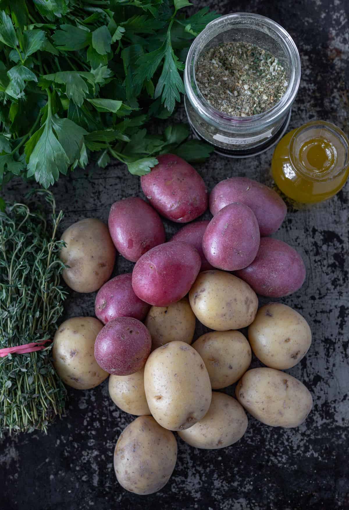 Red and white potatoes surrounding by a bunch of fresh thyme, spices, and oil.