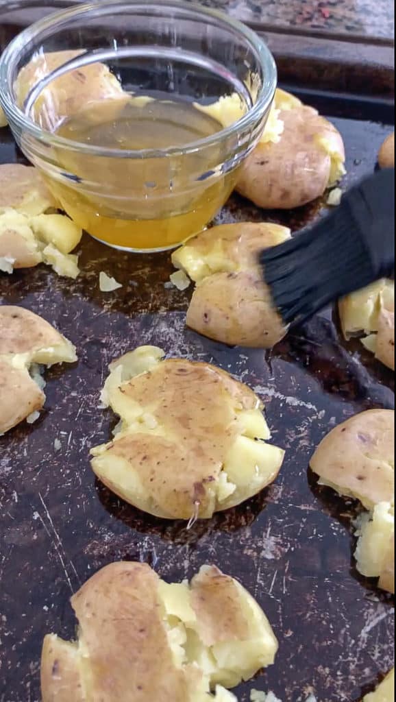 Smashed potatoes being brushed with oil.