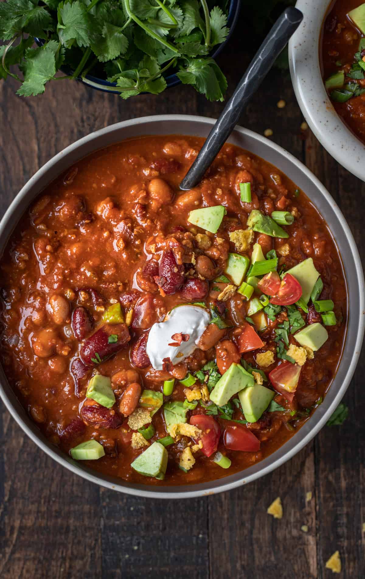 Bowlful of vegan chili topped with avocado, tomatoes, and sour cream.