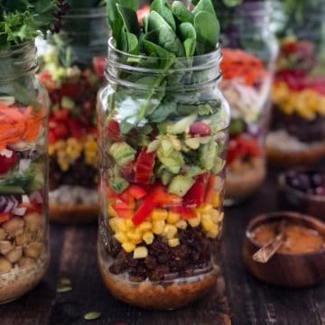Mason jars filled with salad, rice, beans and corn.