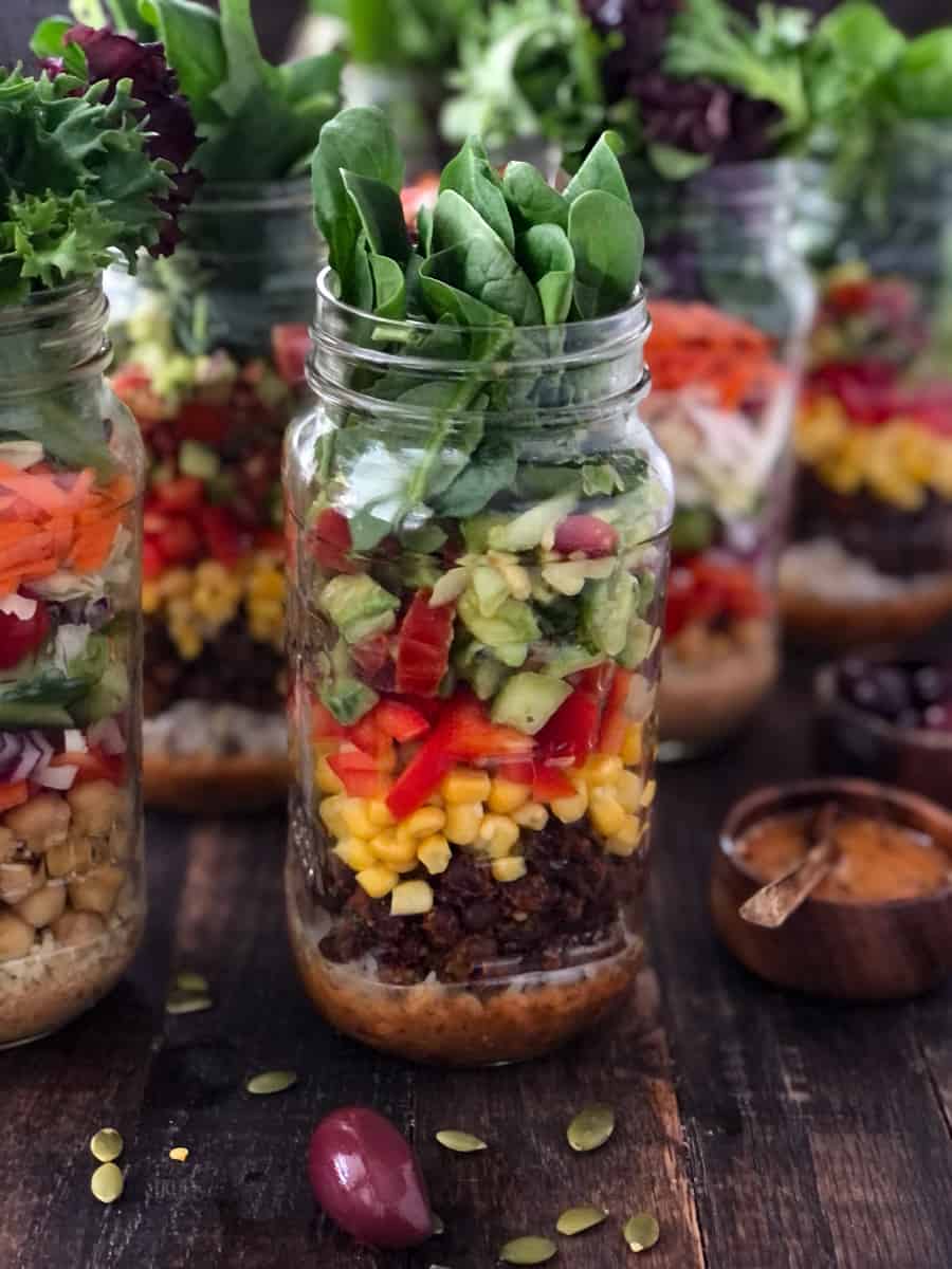 Mason jars filled with salad, rice, beans and corn.