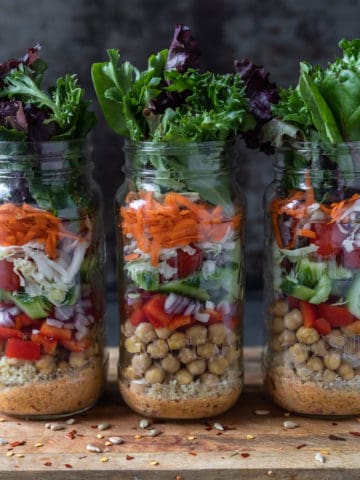 Three jars of salad, rice, beans, and leafy greens.