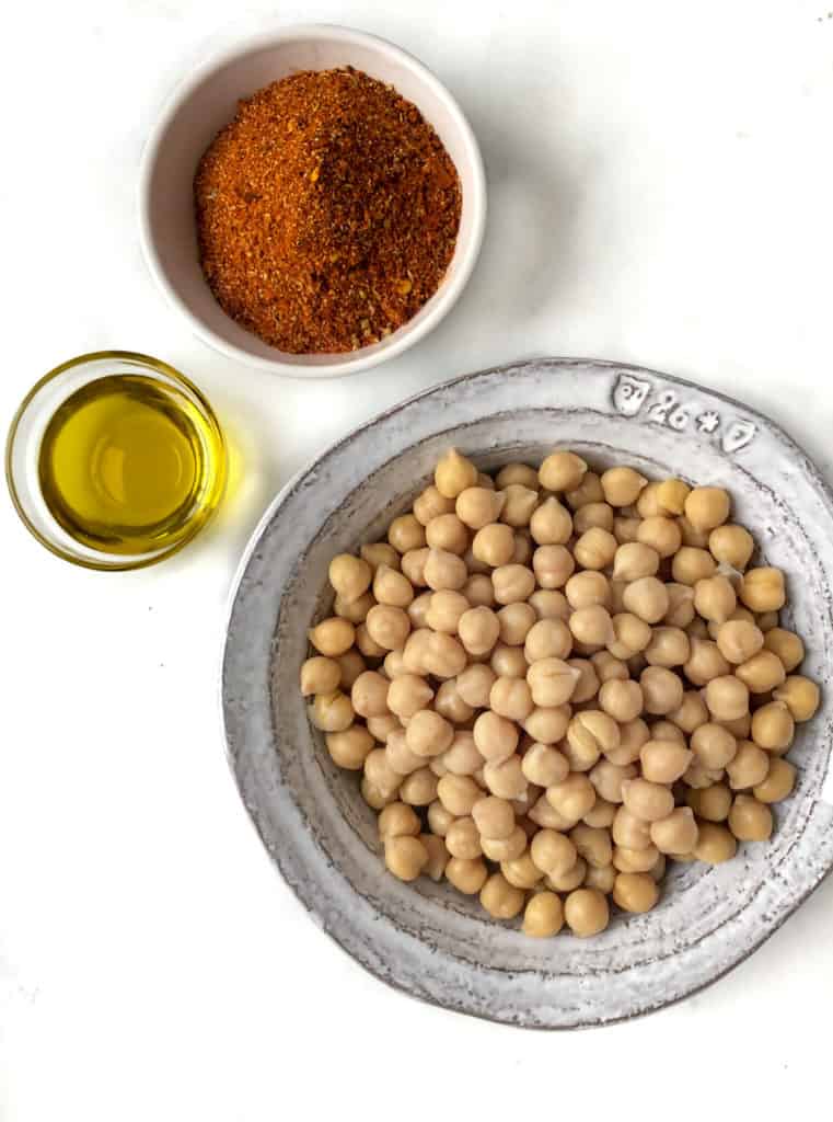Bowls of spices, oil and chickpeas on a table.