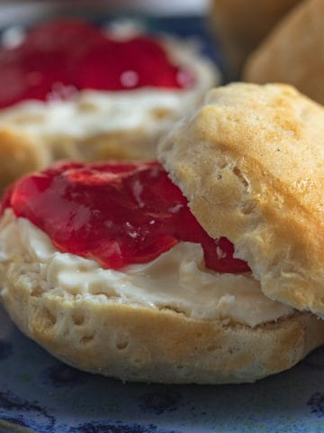 Freshly made biscuit served with butter and jam on a blue plate.
