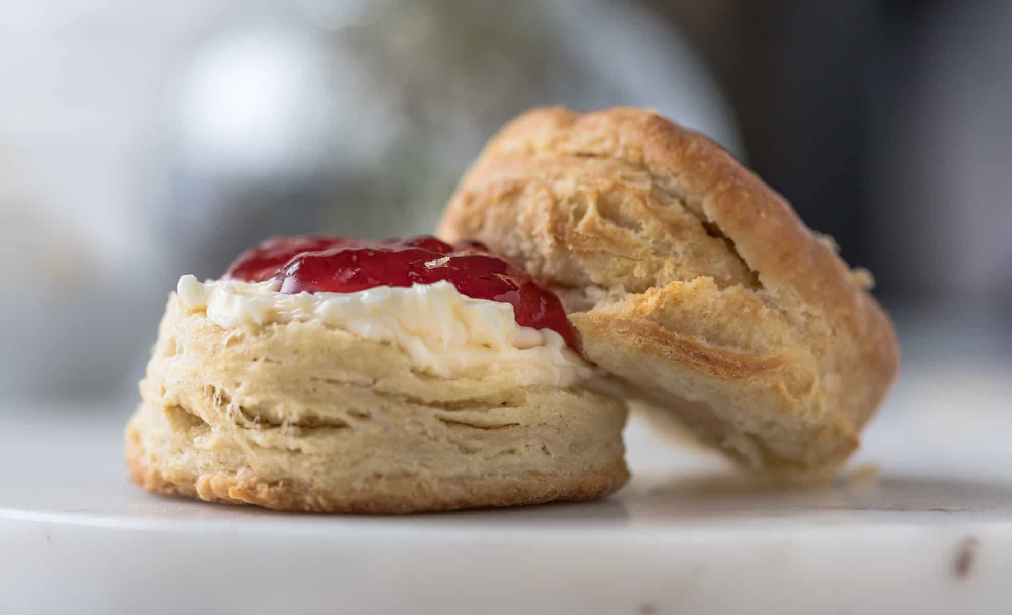 Flaky, fluffy vegan biscuit split in half and slathered with butter and jam.