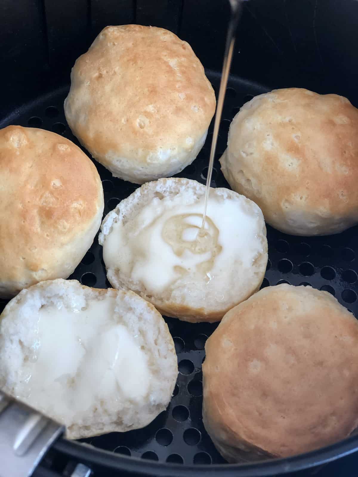 Biscuits in an air fryer slathered in butter with a drizzle of honey.
