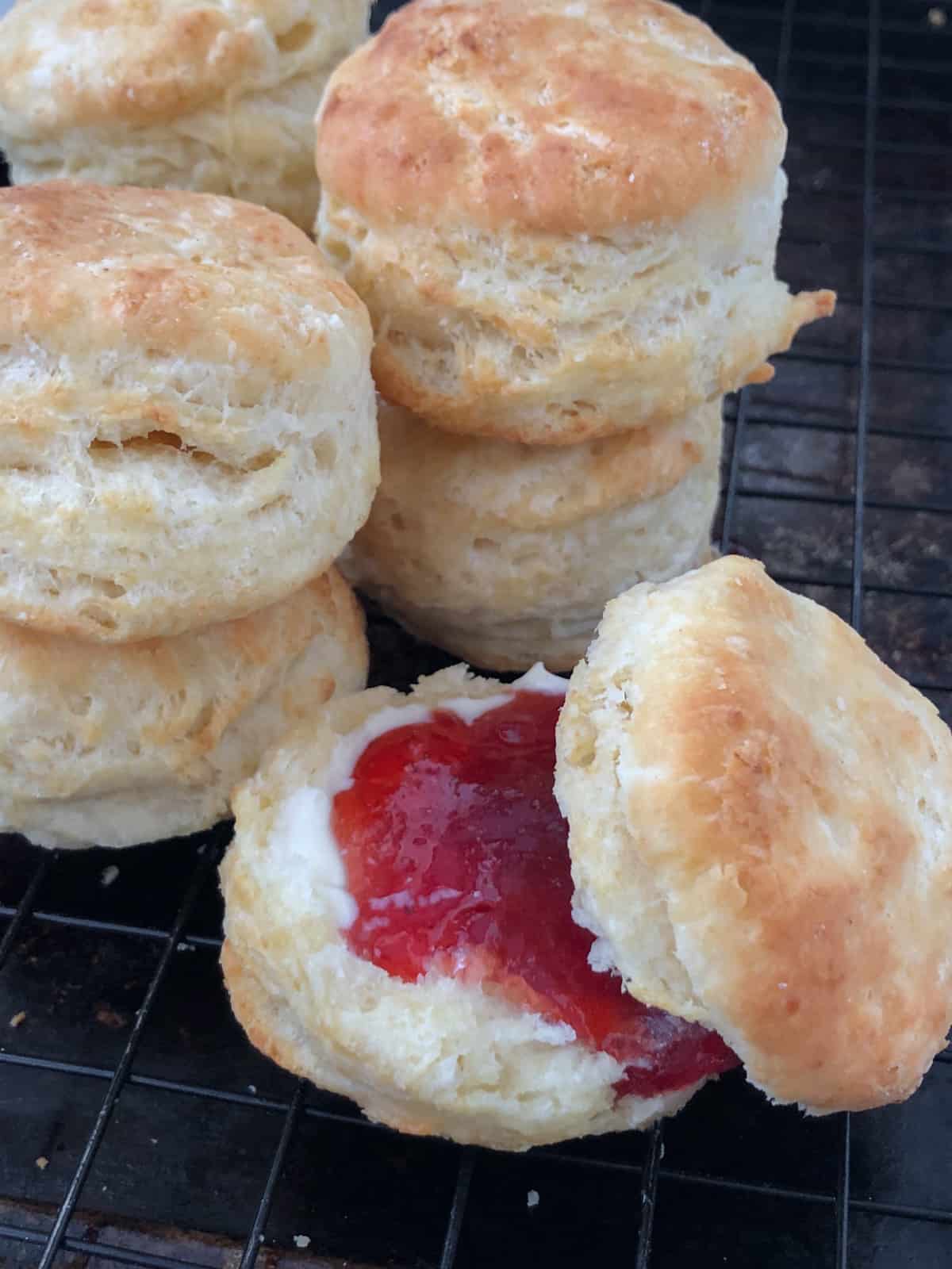 Stack of biscuits on cooling rack with one slather in strawberry jam.