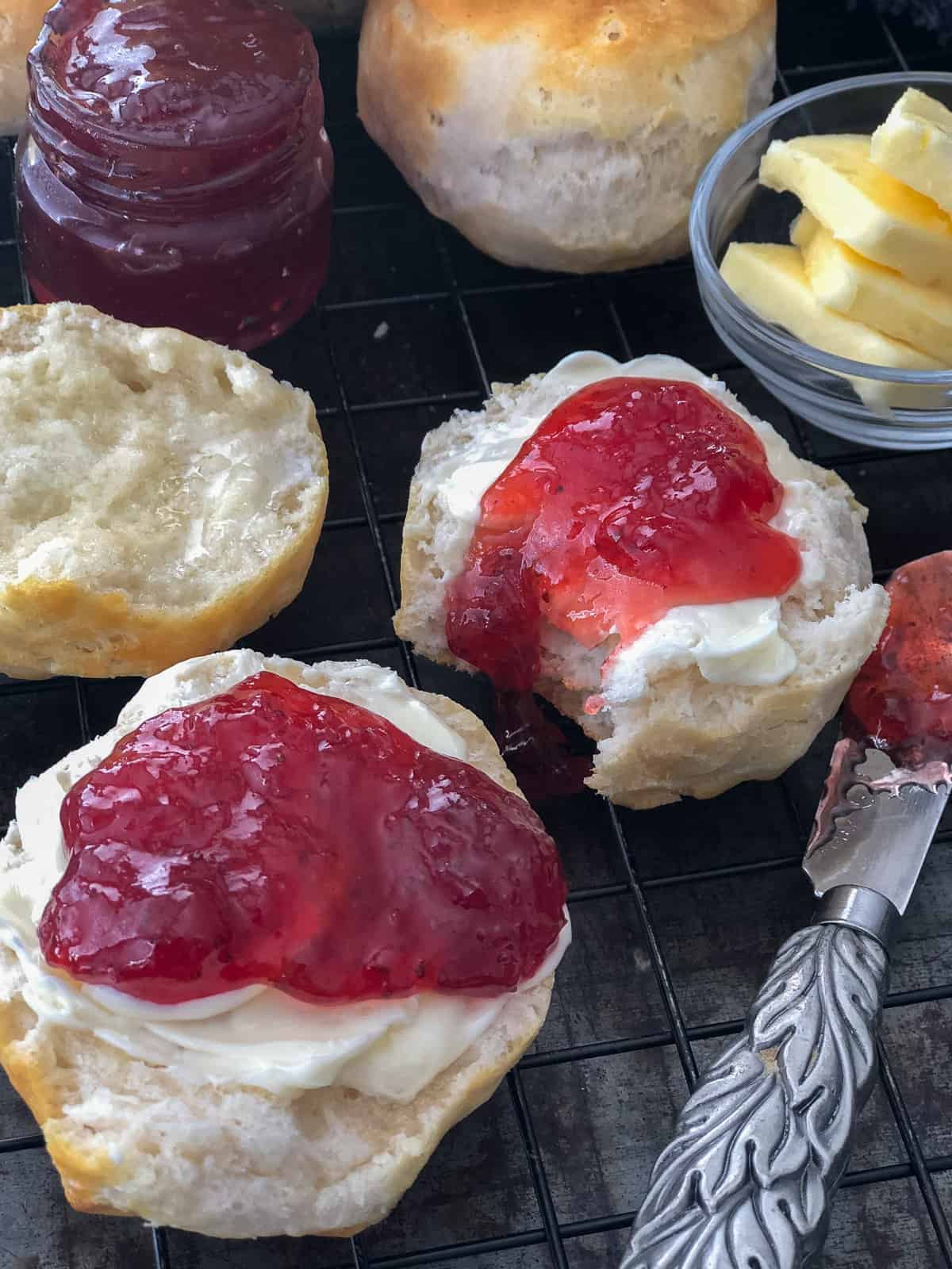 Homemade flaky biscuits covered in butter and jam on a plate.