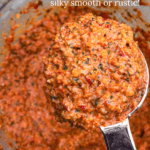 A spoonful of almond and red pepper romesco sauce over a food processor.