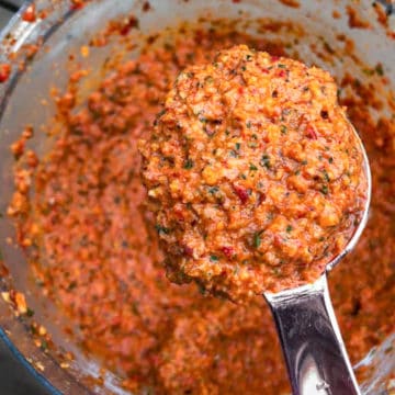 Spoonful of red pepper almond romesco sauce being lifted from food processor.